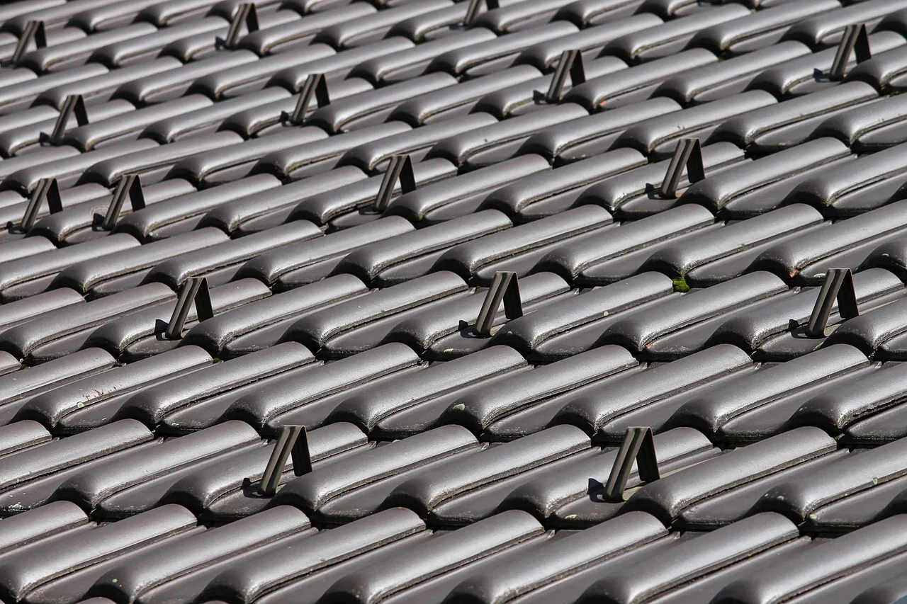 Aufsicht auf eine Deckung aus grauen Betondachsteinen, aus der in regelmaessigen Abstaenden metallische Halter nach oben durch die Deckung treten.