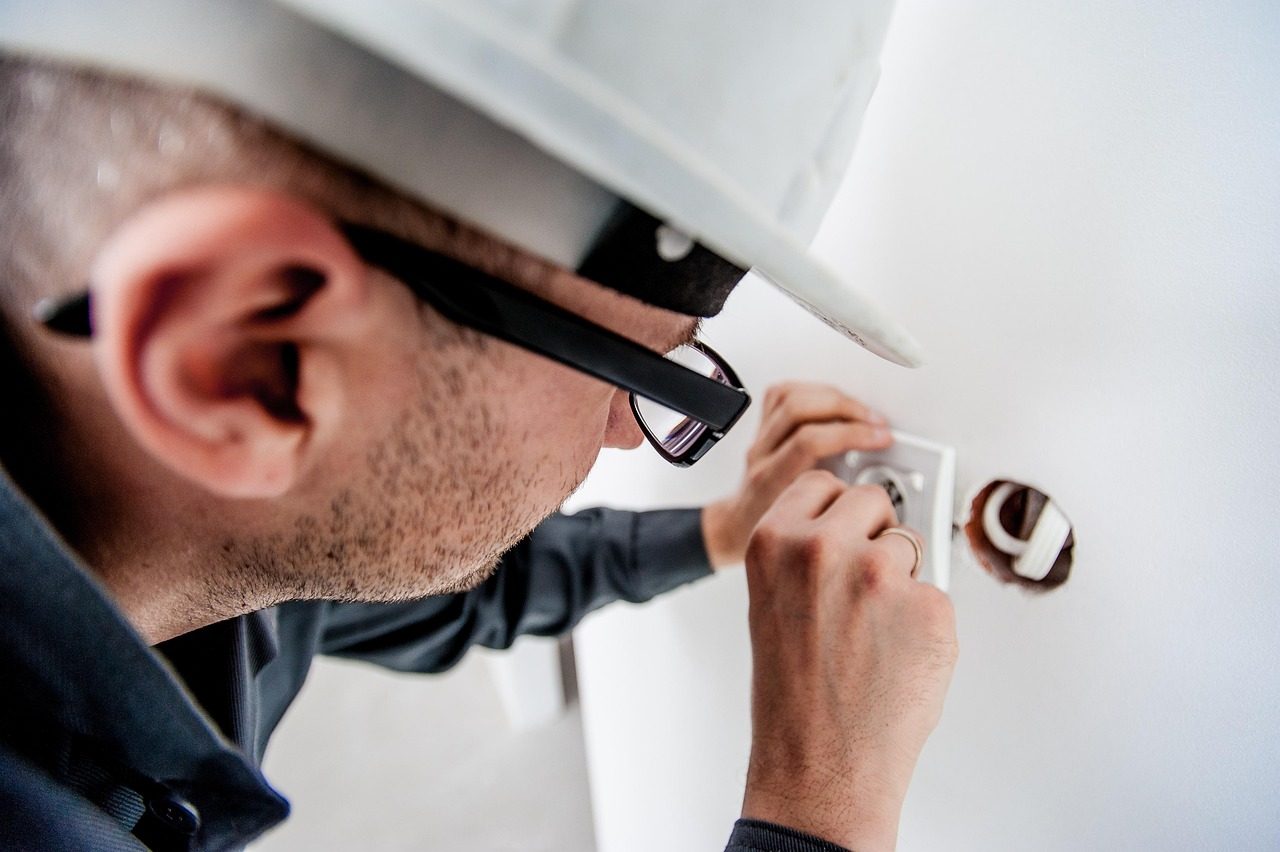 Elektriker mit Schutzhelm bei der Installation einer Steckdose in einer Hauswand